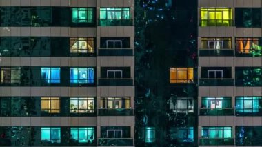 Windows glowing of the multi-storey building of glass and steel lighting and people within timelapse close up view. Dubai, UAE