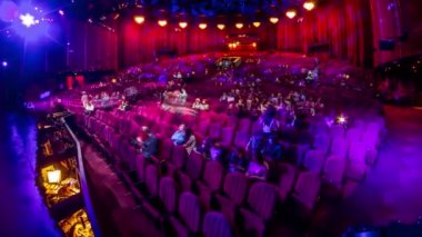Seyirciler konser salonunda toplanıp gösteriyi zaman aşımına uğratarak izliyorlar. Kırmızı koltuklu büyük bir salon. Işığı kapatana kadar izleyiciler yerlerini dolduruyor. Bir sahneden görünüm