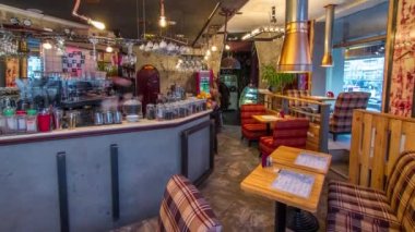 Tezgahı olan modern bir kafe ve zaman ayarlı sandalyeli ahşap masalar. Kahve makineli çay barı ve içecek bardakları.