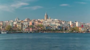 Beyoglu district historic architecture and Galata tower medieval landmark timelapse in Istanbul, Turkey. Many colorful houses reflected in water. Blue cloudy sky at spring sunny day