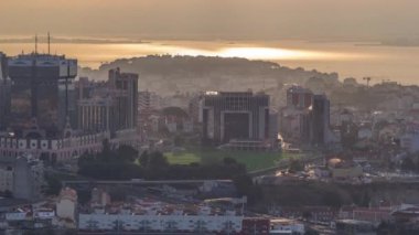 Lisbon during sunrise from viewpoint in Monsanto at morning timelapse. Aerial top view with golden light, colorful clouds and rays of light reflected on river surface and roofs of buildings