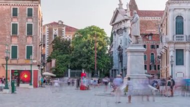 Tourists walking around the monument of Niccolo Tommaseo timelapse on the Campo Santo Stefano city square. Clear summer sky before sunset. Venice, Italy