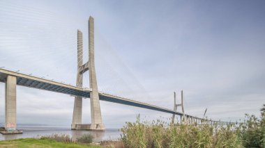 Architectural landmark Vasco da Gama Bridge over the Tagus River in Lisbon, Portugal. Green grass and cloudy sky. The longest bridge in the European Union.