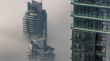 Dubai Marina ufuk çizgisi üzerinde nadir bulunan kış sisi ve hava saatleri üzerinde cam gökdelenlerle kaplı kuleler. Üst görünüm bulutların üstünde. Dubai, BAE