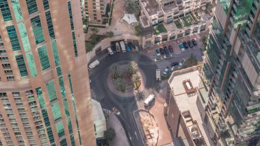 Aerial look down view of a circle road intersection between skyscrapers with shadows moving fast in a big city. Urban landscape of Dubai Marina district in UAE with cars and parking near supermarket