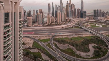 Dubai Marina karayolu kavşağındaki panorama spagetti kavşağı gece gündüz geçiş zamanı. Arka planda en uzun gökdelenler aydınlatılıyor. Güneş doğmadan önce JLT bölgesinden hava üst görünümü