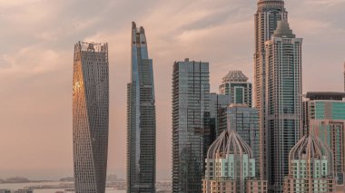 Dubai Marina 'nın en yüksek konutlu gökdelenleri gün batımında, cam bir yüzeyden yansıyan güneş ile birlikte zaman çizelgeleriyle. JLT bölgesinden hava üst görünümü