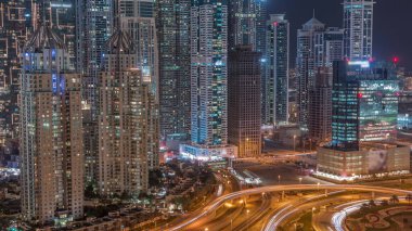Dubai Marina 'da büyük bir karayolu kavşağında hava manzarası var. Çevrede gökdelenler var, BAE. JLT bölgesinden araba trafik görüntüsü. Pencerelerinde ışık olan aydınlık kuleler