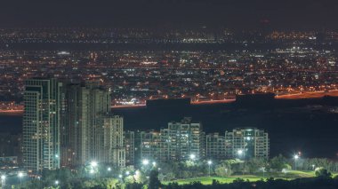 Dubai marinasından yeşilliklerin hava görüntüsü gece saat dilimi. Yukarıdan caddelerde trafik olan kuleler ve gökdelenler. Arka planda ve golf sahasında villalar