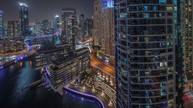 Panorama Dubai marinasının hava manzarasını gösteriyor. Kanal etrafındaki gökdelenleri aydınlatıyor. Yüzen yatlar ve gece saatleri var. Jlt ve JBR bölgelerindeki kuleler. Yat kulübünde beyaz tekneler var.