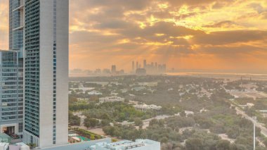 Zabeel bölgesinin bahçesinde gün doğumu, arka planda gökdelenler, Dubai, BAE 'de hava zaman aralığı. Gökyüzünde turuncu bulutlar ve güneş ışığı