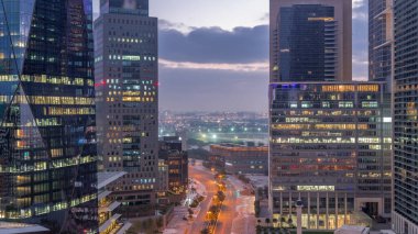 Dubai International Financial district night. Aerial view of business office towers before sunrise. Illuminated skyscrapers with road traffic and Deira district on a background
