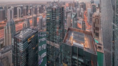 Dubai Marina ve JLT ilçelerinde gökdelenler arasında karayolu trafiği gece gündüz geçiş zamanı. Gündoğumundan önce aydınlatılmış modern kuleler ve inşaat alanı panoramik görünümü