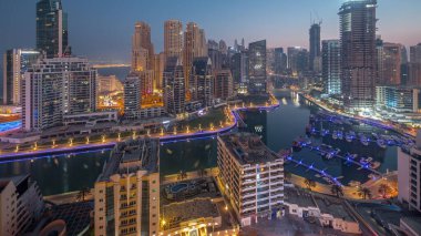 Limanda park etmiş tekne ve yatları olan Dubai Marina ve gün doğumundan önce gece gündüz kanal havası etrafında gökdelenler aydınlatılıyor. Arka planda JBR bölgesi kuleleri