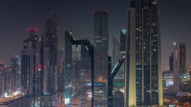 Dubai Finansal Merkezi 'nin tüm gece boyunca ışıkların sönmesiyle aydınlanan yüksek gökdelenleri ile yakın görüntüsü. Yoğun karayolu boyunca kulelerin hava görüntüsü