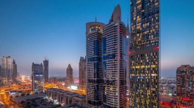Günbatımından sonra Dubai Uluslararası Finans Bölgesi 'nin hava görüntüsü ve birçok gökdelen gece gündüz geçiş zamanı. Otoparkın yanındaki kavşakta trafik vardı. Dubai, BAE.