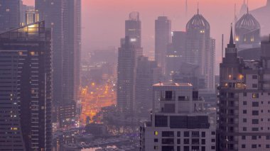 Dubai Marina ve Media City semtleri modern gökdelenler ve ofis binaları gece gündüz geçiş zamanları. Limandaki yatların yakınındaki üst geçitte trafik ve kavşak.