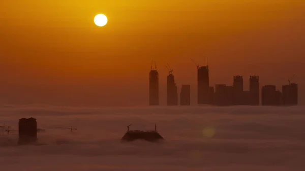 迪拜湾上空的日出 摩天大楼和塔楼被晨雾笼罩 空中飞驰而过 大红太阳在建筑物和橙色的天空后面升起 — 图库照片