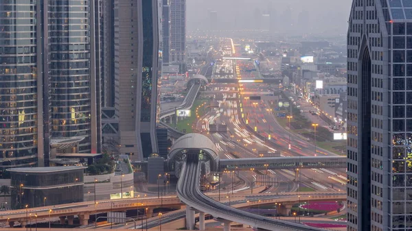 Busy Sheikh Zayed Road aerial day to night transition timelapse, metro railway and modern skyscrapers around in luxury Dubai city. Heavy traffic on a highway with many cars. United Arab Emirates