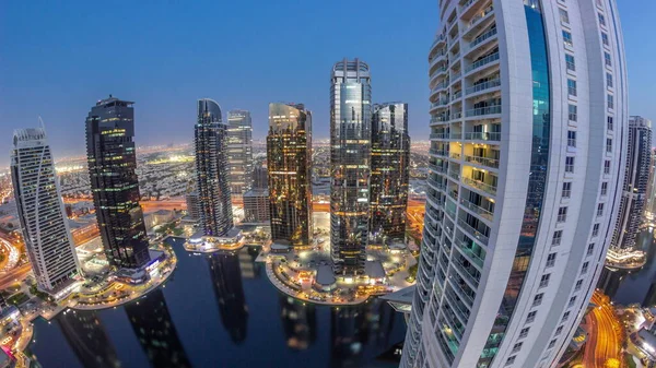 Tall residential buildings panorama at JLT district aerial day to night transition timelapse, part of the Dubai multi commodities centre mixed-use district. Skyscrapers around pond