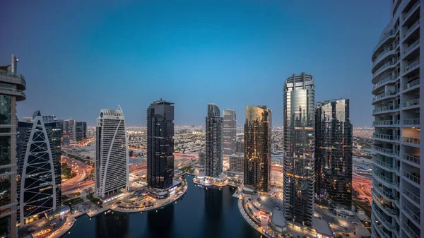 Tall residential buildings at JLT district aerial day to night transition timelapse, part of the Dubai multi commodities centre mixed-use district. Panoramic view to towers and skyscrapers