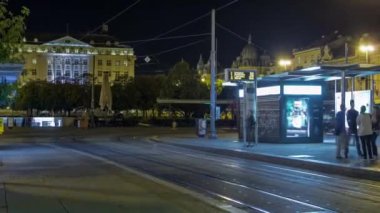 New modern trams of Croatian capital Zagreb night timelapse near railway station. People at tram stop at evening time. CROATIA