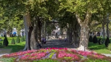 People walking around pavillion in Zrinjevac park timelapse in Zagreb, Croatia. Zrinjevac is spread over 12540 sq meters in city center. Flowerbed on foreground