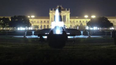People on the Tomislav Square with fountain in front of Main Railway Station night timelapse, main hub of Croatian Railways network. People on a bench. Zagreb, Croatia