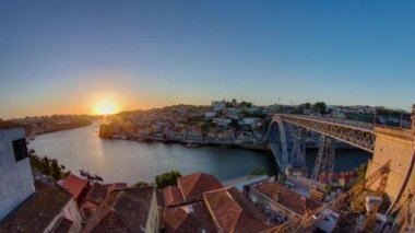 Panorama of old city Porto at river Duoro, with Port transporting boats at sunset timelapse with the Dom Luiz bridge, Oporto, Portugal. Red roofs of historic buildings