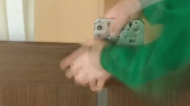 Close-up carpenter hands in green uniform with doorlock during lock process installation into brown wood door timelapse