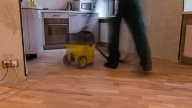 Yeşil üniformalı marangoz işçileri yer döşeme çalışma saatleri sırasında parke tahtası yerleştirdikten sonra elektrikli süpürgeyle oturma odasını temizliyorlar..