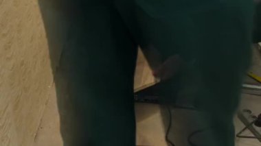 Yeşil üniformalı marangoz, yerdeki tahta paneli testere ile kesiyor.