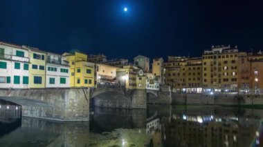 İtalya 'nın Floransa kentindeki Arno nehrinin üzerindeki ünlü Ponte Vecchio köprüsü zaman atlaması gece aydınlandı. Dolunay yükseliyor. Suyun yansıması. Yan taraftaki eski evler