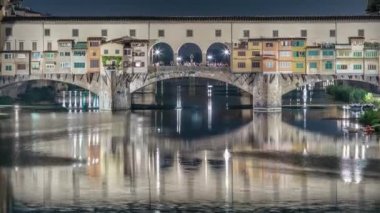 Floransa 'daki Arno nehrinin üzerindeki ünlü Ponte Vecchio köprüsü gece aydınlandı. Suyun yansıması. Yan taraftaki eski evler