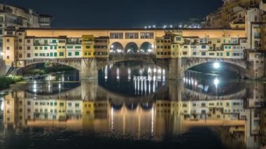 İtalya 'nın Floransa kentindeki Arno nehrinin üzerindeki ünlü Ponte Vecchio köprüsünün zaman çizelgesi gece aydınlandı. Suyun yansıması. Yan taraftaki eski evler