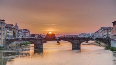 Floransa 'da günbatımında ünlü Kutsal Üçlemeci Köprüsü zaman çizelgesiyle Arno nehrinin yukarısından şehir manzarası. Sudaki yansımalar. Turuncu gökyüzü