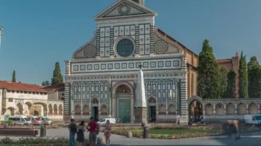 Santa Maria Novella Bazilikası Floransa 'da homonym kare zaman diliminde. Önünde çiçek tarlaları ve yeşil çimenler var. İnsanlar bankta oturuyor. Yazın mavi gökyüzü