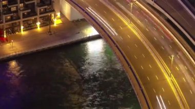 Dubai Marina 'da gece hava manzarası, botlarla kanal ve otelin yakınındaki trafik saatleriyle köprü. Yukarıdan aydınlatılmış rıhtıma bak