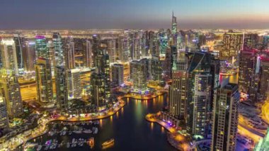 Dubai Marina 'da yatlar ve gece gündüz hava geçiş panoramik zaman dilimi. Mavi gökyüzü ile açık bir akşamda parlak ışıklar ve en yüksek gökdelenler. Gün batımından sonra yukarıdan görünüm