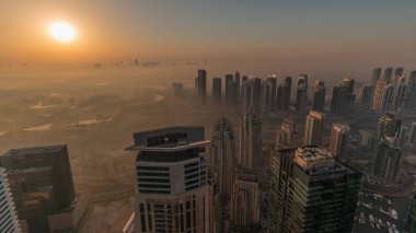 Panorama of Dubai Marina with JLT skyscrapers and golf course during sunrise , Dubai, United Arab Emirates. Aerial view from above towers foggy morning. City skyline with orange sky