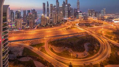 Panorama of Dubai Marina highway intersection spaghetti junction day to night transition . Illuminated tallest skyscrapers on a background. Aerial top view from JLT district after sunset