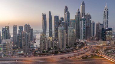 Dubai Marina 'nın gökdelenleri, gün batımından sonra gün batımından sonra karayolu trafiğiyle aydınlık konutlu binalar. JLT bölgesinden hava üst görünümü
