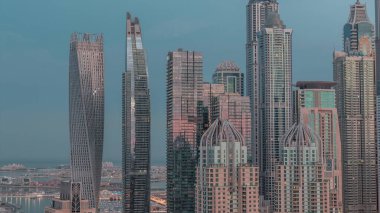 Skyscrapers of Dubai Marina with illuminated highest residential buildings night to day transition . Aerial top view from JLT district. Sun reflected from glass during sunrise