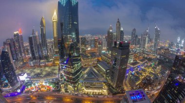 Panorama of futuristic skyscrapers after sunset in financial district business center in Dubai with traffic on a road day to night transition . Aerial view from above with cloudy sky