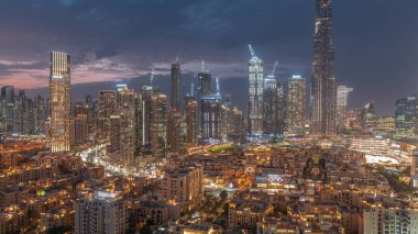 Dubai Downtown day to night transition  with tallest skyscraper and other towers around old town view from the top after sunset in Dubai, United Arab Emirates. Lights turning on.