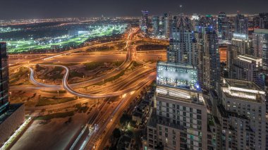 Panorama showing Dubai marina and JLT illuminated skyscrapers along Sheikh Zayed Road with huge junction and media city district aerial night . Residential and office buildings from above.