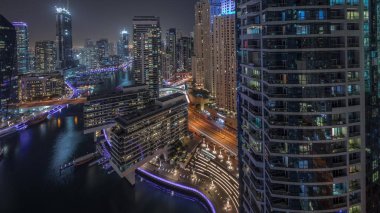 Panorama showing aerial view to Dubai marina illuminated skyscrapers around canal with floating yachts night . Towers in jlt and jbr districts. White boats are parked in yacht club