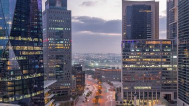 Dubai International Financial district night to day transition . Aerial view of business office towers before sunrise. Illuminated skyscrapers with road traffic and Deira district on a background