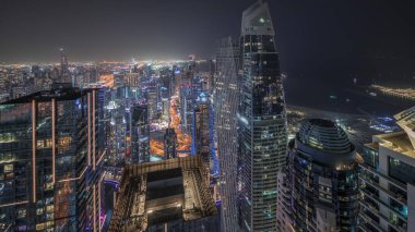 Panorama showing JBR district and Dubai Marina with JLT. Traffic on highway between skyscrapers aerial night . Illuminated modern towers and construction site