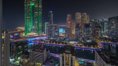 Panorama showing Dubai Marina skyscrapers and JBR district with luxury buildings and resorts aerial night . Illuminated waterfront and boats floating in canal